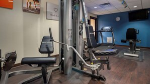 A hotel fitness center with various exercise machines, a treadmill, and a television on the wall. - Comfort Suites Mobile (Mobile)