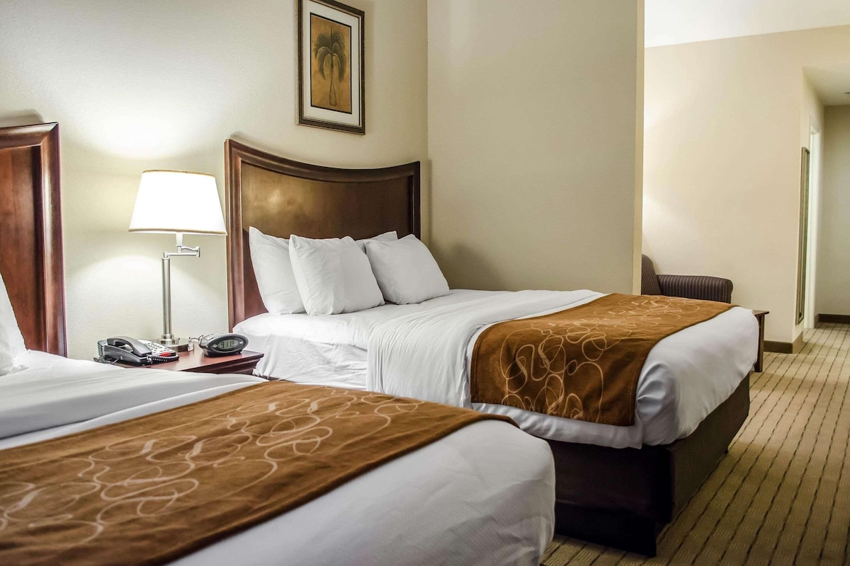 Una camera d'albergo con due letti, un comodino con lampada e telefono, un quadro appeso al muro e una poltrona.