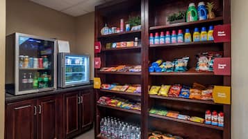 Una estación autoservicio de bebidas con un refrigerador y un congelador, provista de diversas bebidas y aperitivos.