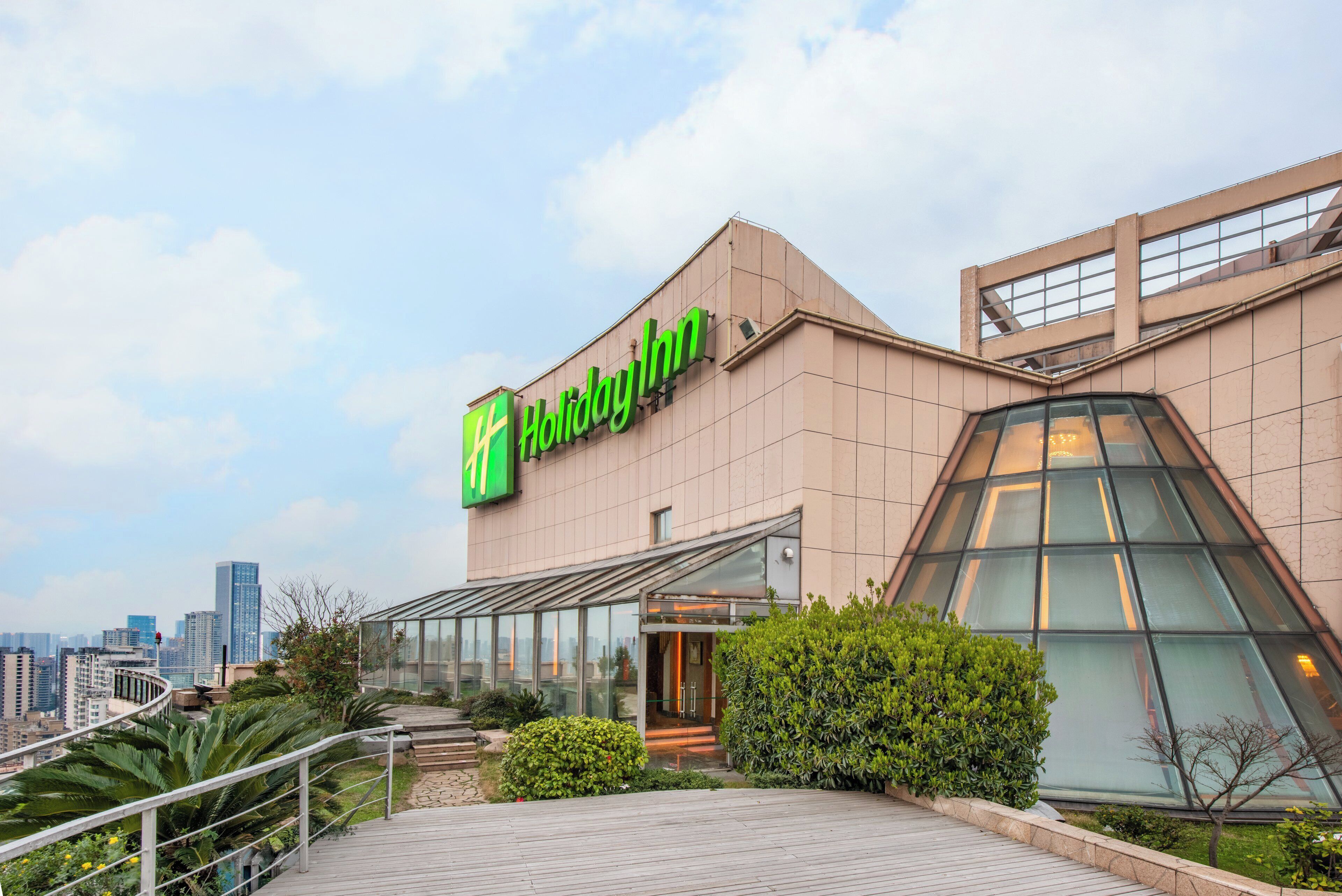 Un hotel Holiday Inn con fachada moderna, amplia entrada de vidrio y jardín en la azotea.