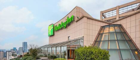 Un hotel Holiday Inn con fachada moderna, amplia entrada de vidrio y jardín en la azotea.