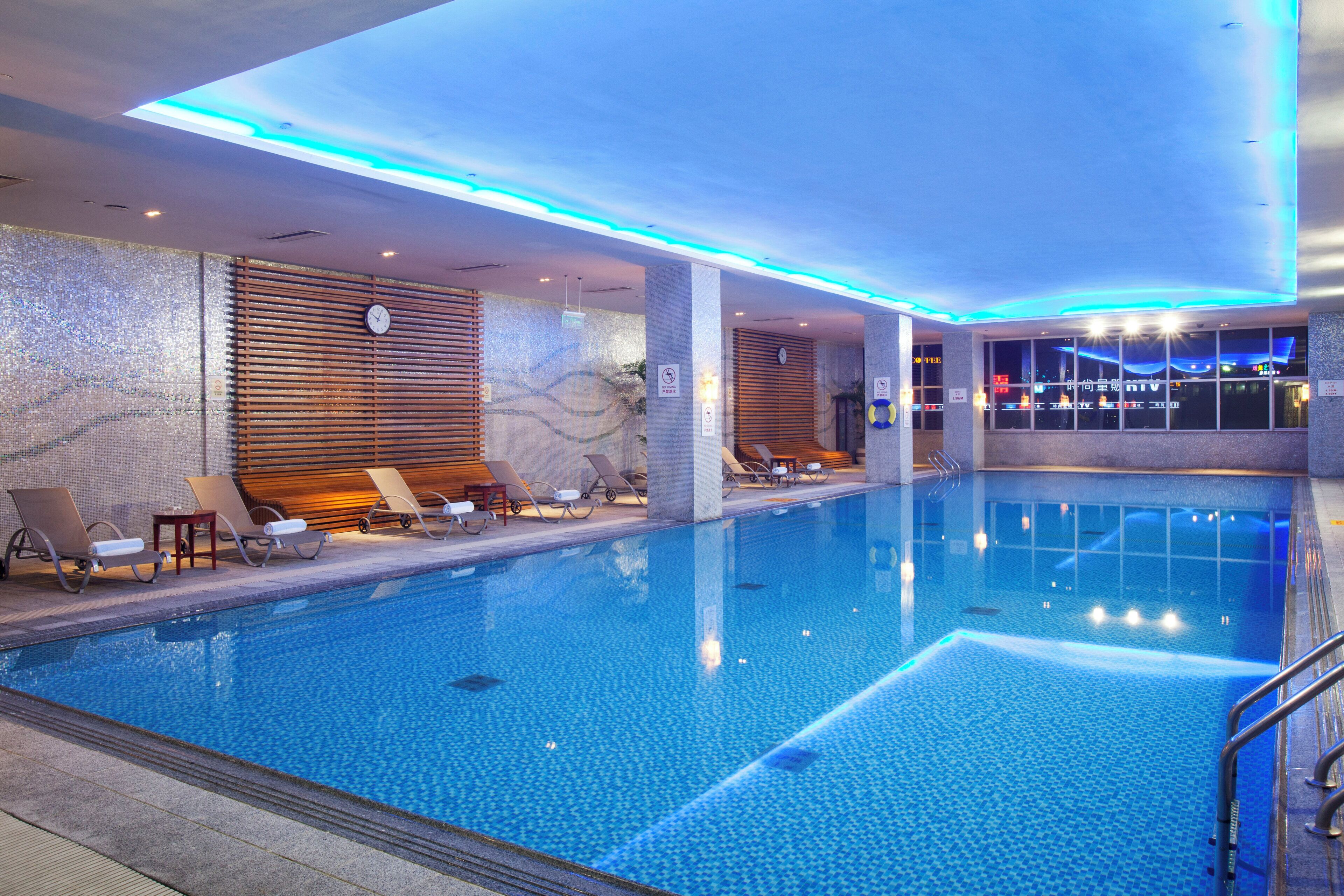 A swimming pool with lounge chairs and a clock on the wall.