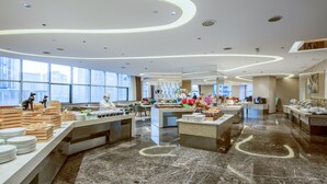 A modern hotel dining area with marble floors, large windows, and a buffet setup.