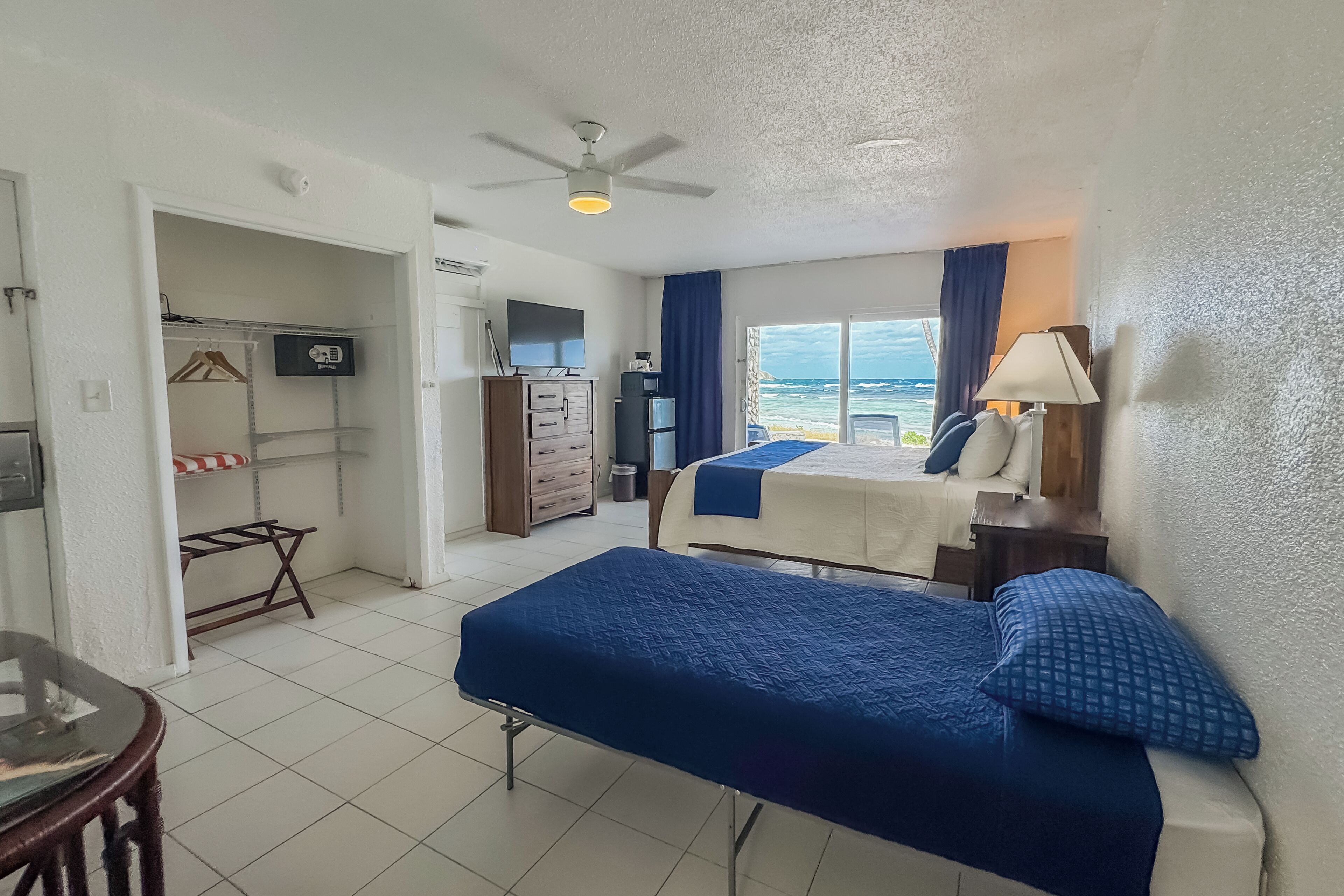 A hotel room with a bed, a desk, a chair, a wardrobe, a television, and a view of the sea.