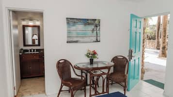 A dining area with a table and chairs, a painting of a beach scene, and a door leading outside.