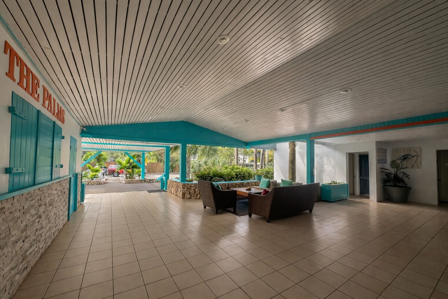A spacious indoor area with a tiled floor, a covered seating area with chairs and a table, and a view of the outside through large windows.