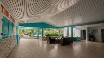 A spacious indoor area with a tiled floor, a covered seating area with chairs and a table, and a view of the outside through large windows.
