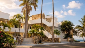 Un resort con fachada de piedra, palmeras y una escalera que conduce a un edificio blanco.