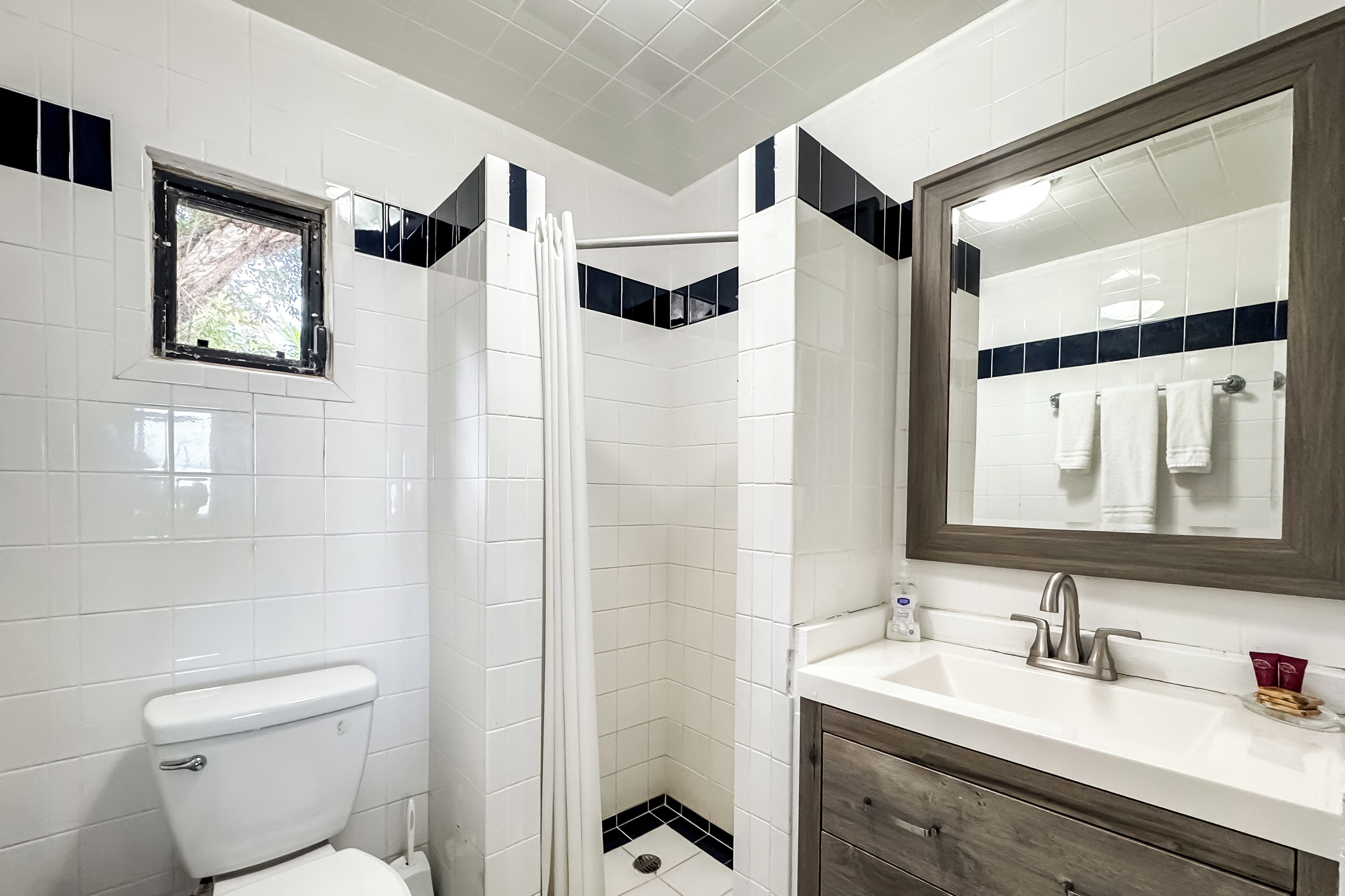 A bathroom with a toilet, a shower with a curtain, a sink with a mirror, and a window.