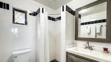 A bathroom with a toilet, a shower with a curtain, a sink with a mirror, and a window.