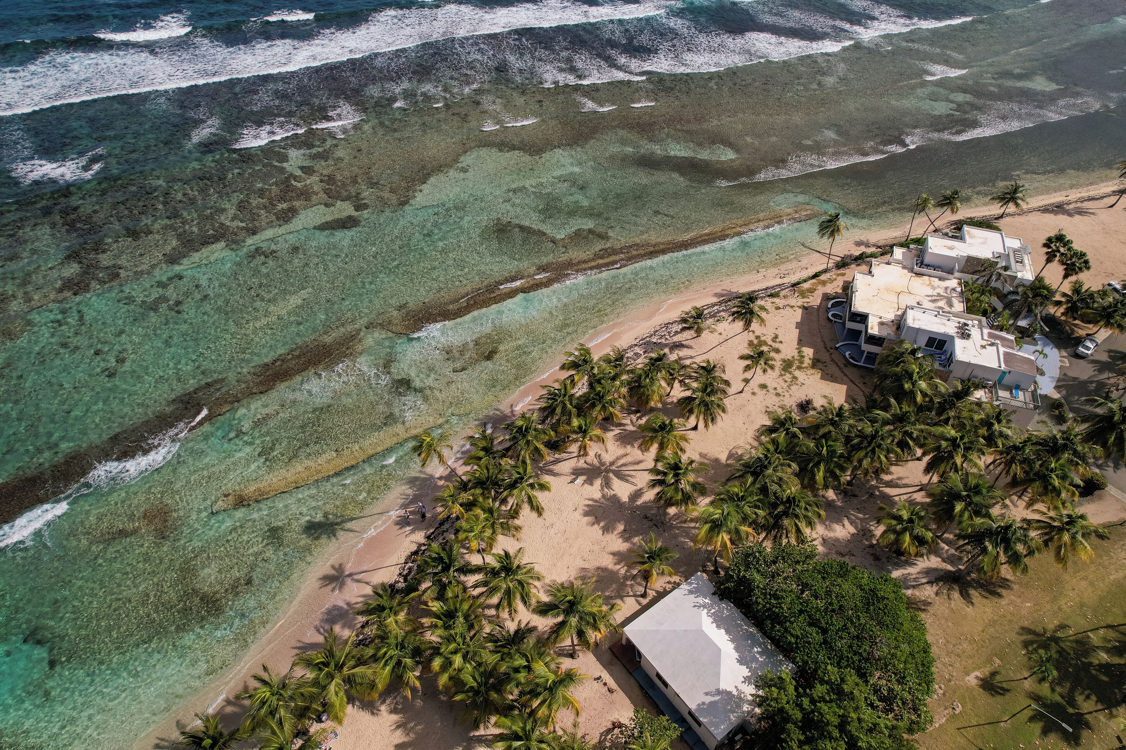 An aerial view of a beachside property with clear turquoise waters, a sandy beach, and palm trees.
