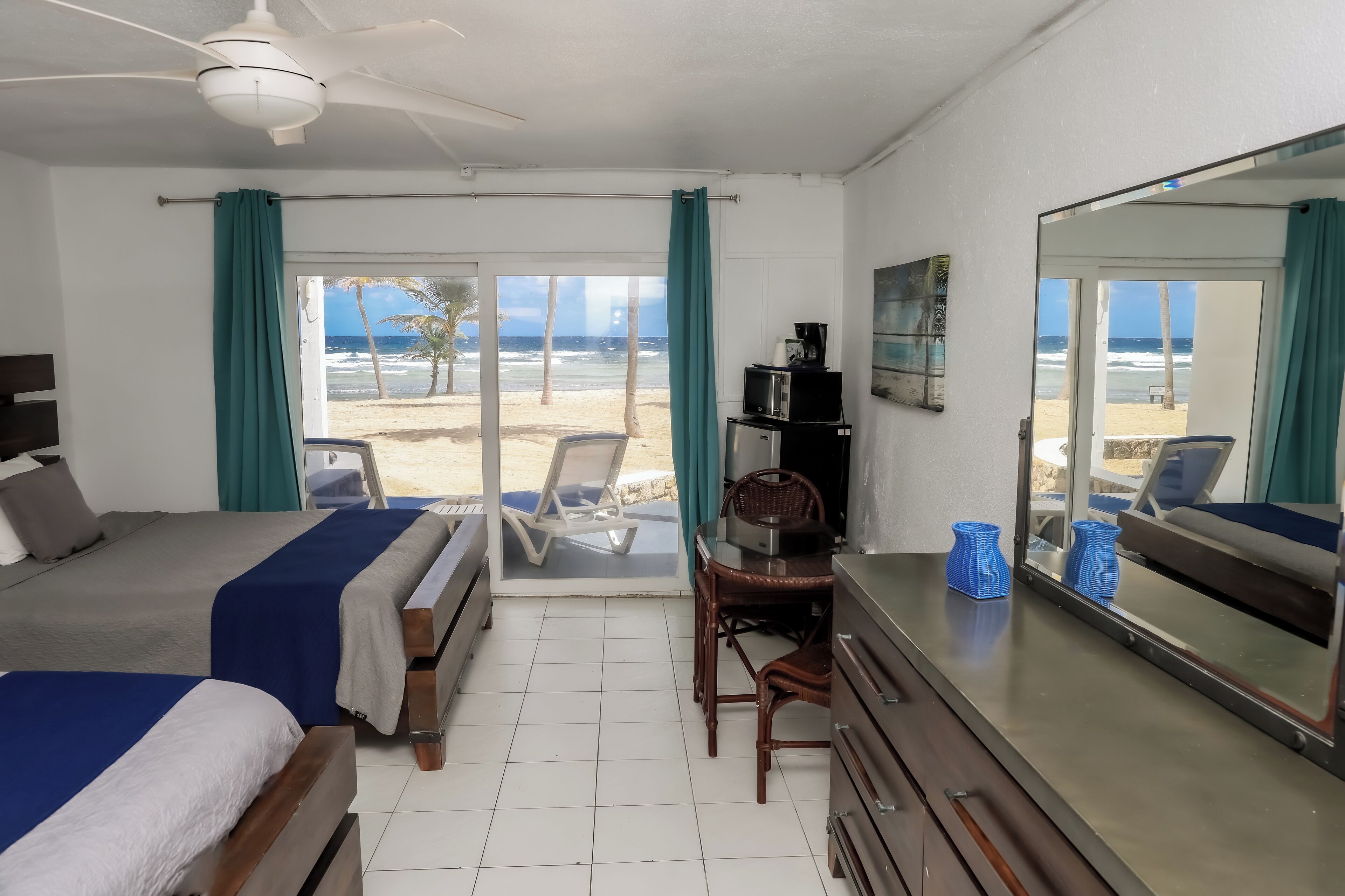 Une chambre d’hôtel avec deux lits, un bureau, une chaise, un grand miroir et une vue sur la plage.