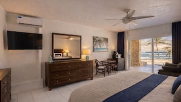 A hotel room with a bed, a desk, a chair, a television, a ceiling fan, and a view of the beach.