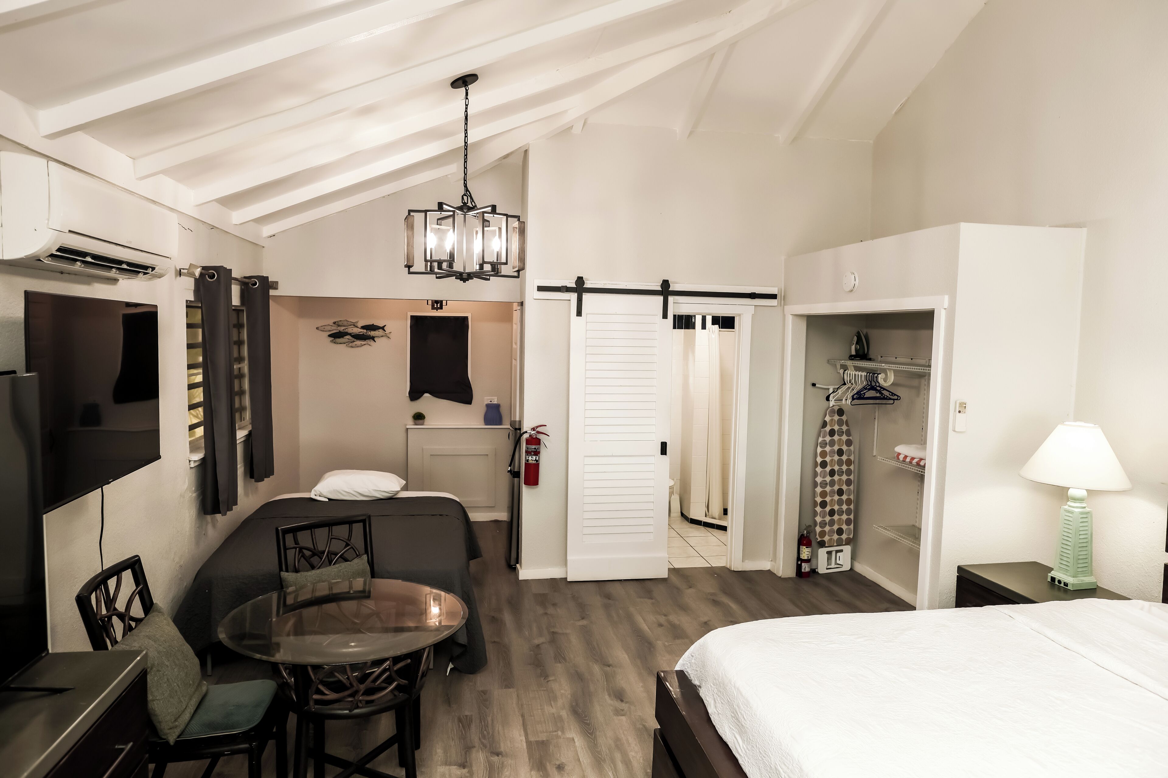 Quarto de hotel com cama, mesa de jantar com cadeiras, televisão, guarda-roupa e armário.