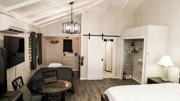 Quarto de hotel com cama, mesa de jantar com cadeiras, televisão, guarda-roupa e armário.