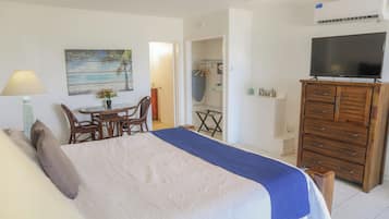 A bedroom with a bed, a TV on a wooden cabinet, a painting, and a small table with chairs.