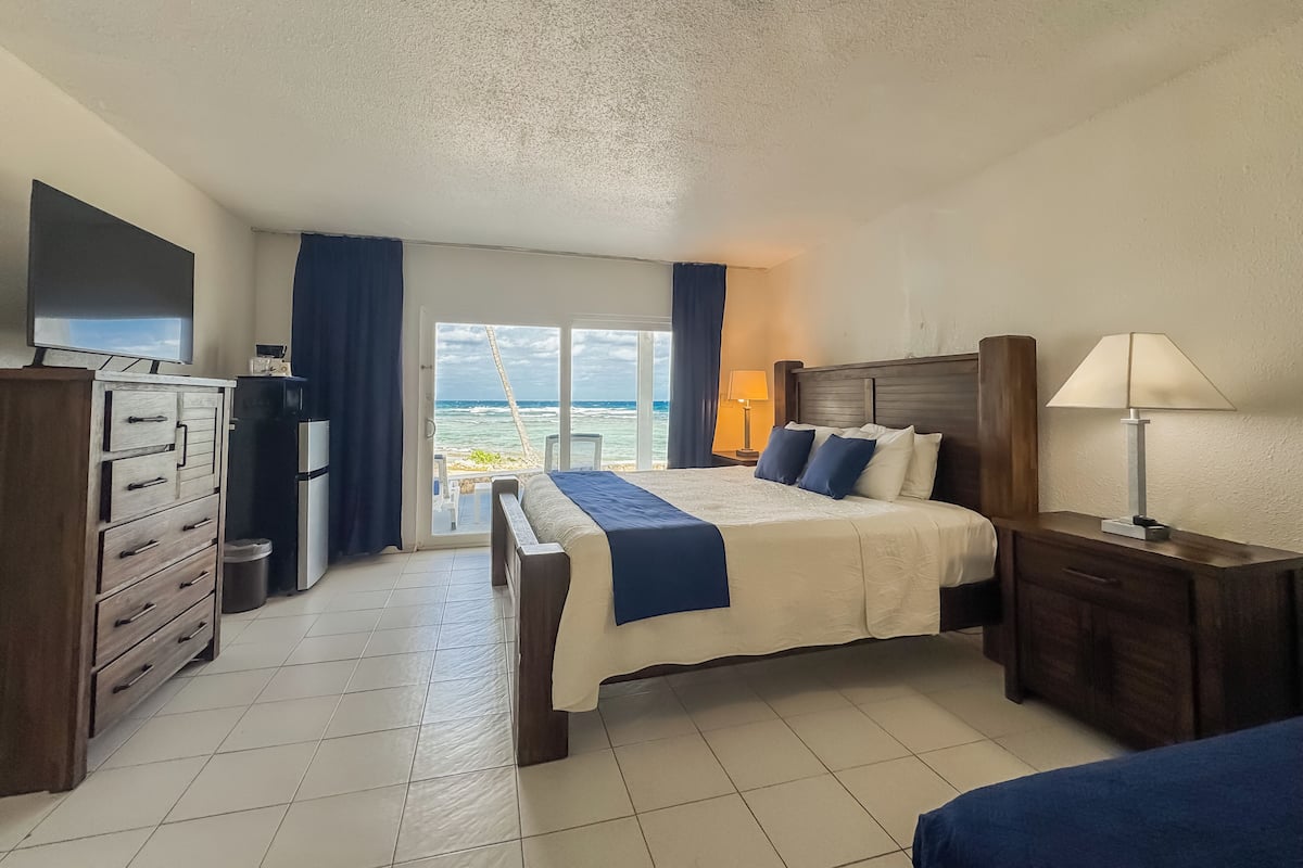 Une chambre d’hôtel avec un lit, une commode, une télévision, une lampe et une vue sur l’océan.