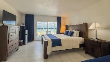 A hotel room with a bed, a dresser, a TV, a lamp, and a view of the ocean.