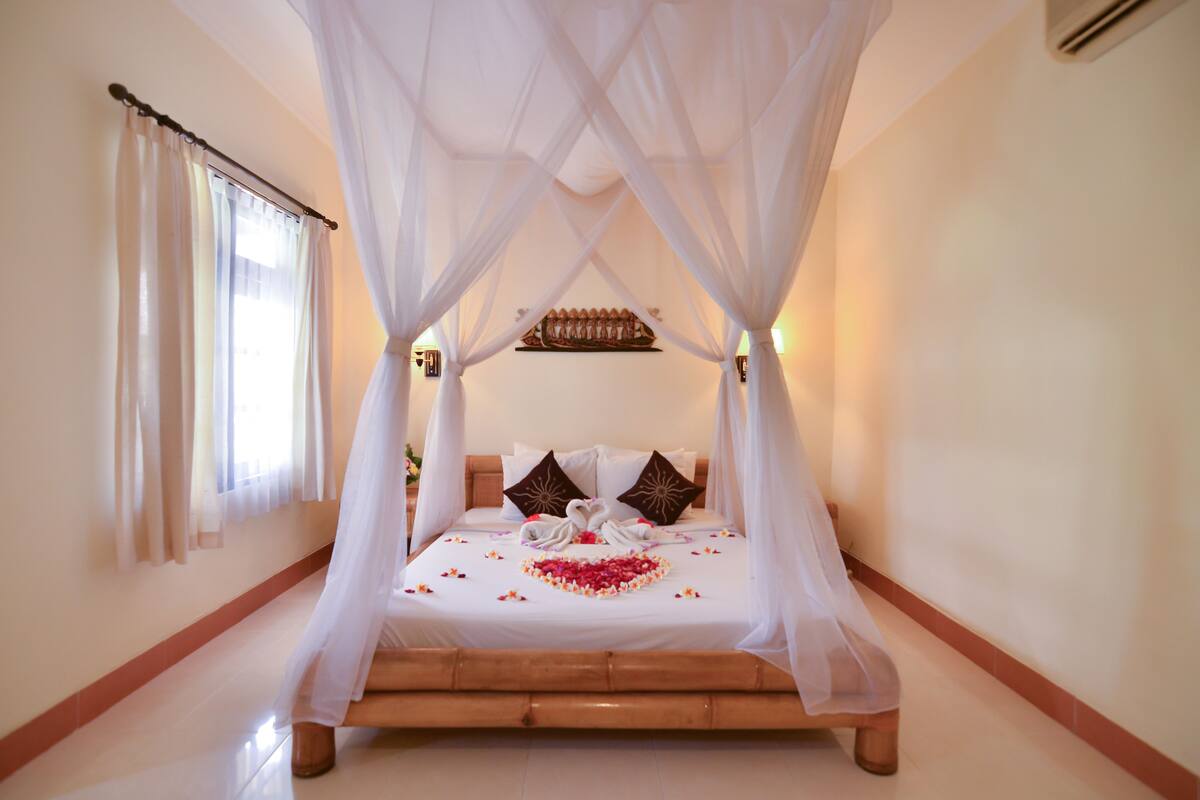 Una cama con dosel, ropa de cama blanca y un adorno con forma de corazón sobre la cama.