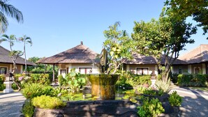 Un resort con edificios de techo de paja, un elemento acuático central y exuberante jardinería tropical.