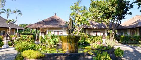 A resort with thatched-roof buildings, a central water feature, and lush tropical landscaping.