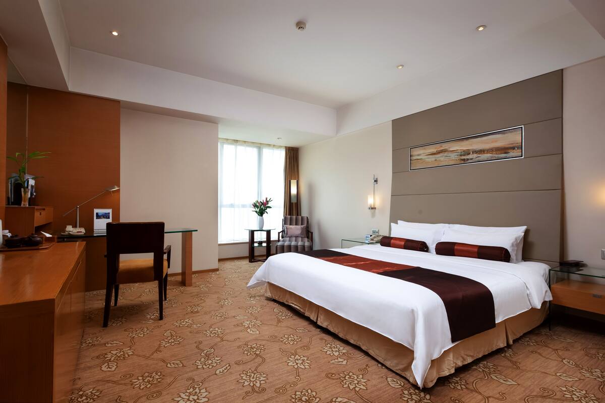 Een hotelkamer met een groot bed, een bureau, een stoel en een tafeltje met een bloemenvaas.