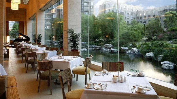 Ravintola, jossa on ruokailua varten katetut pöydät, ja suurista ikkunoista avautuu näkymä vesiaiheeseen ja ympäröiviin rakennuksiin.