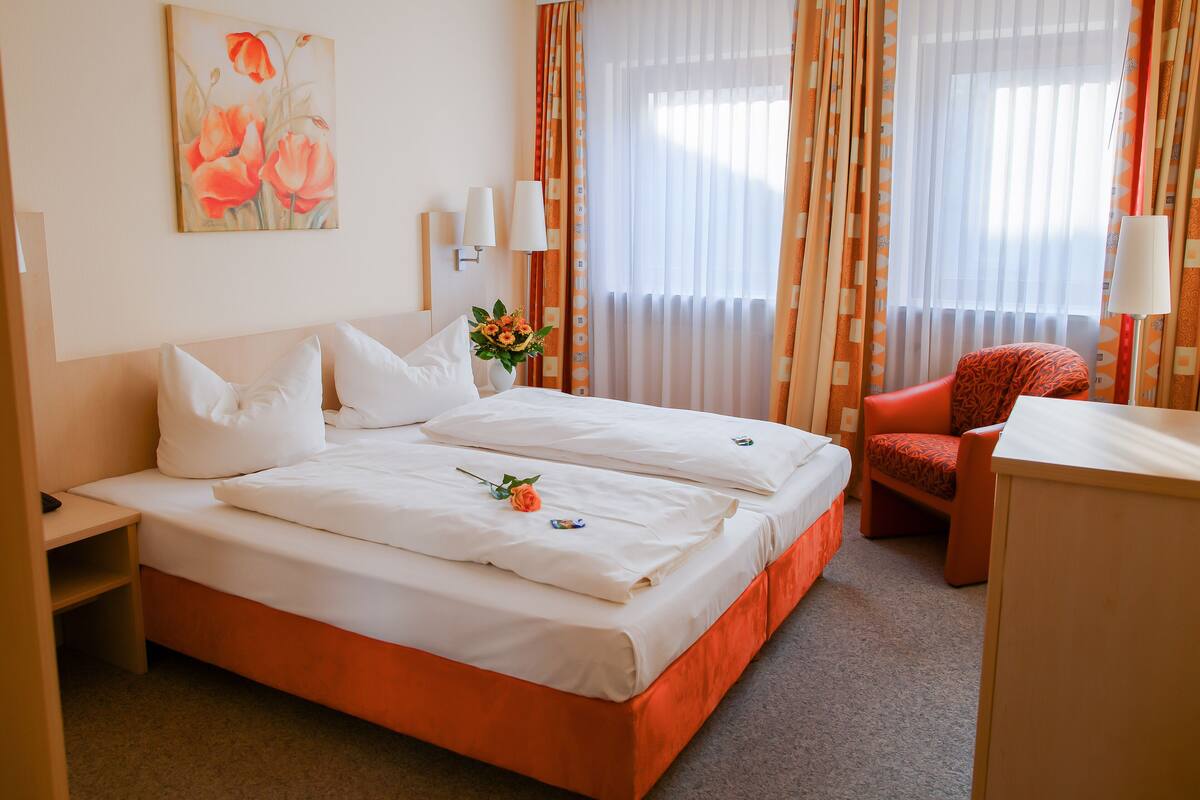 A hotel room with a double bed, a desk, a chair, and a painting on the wall.
