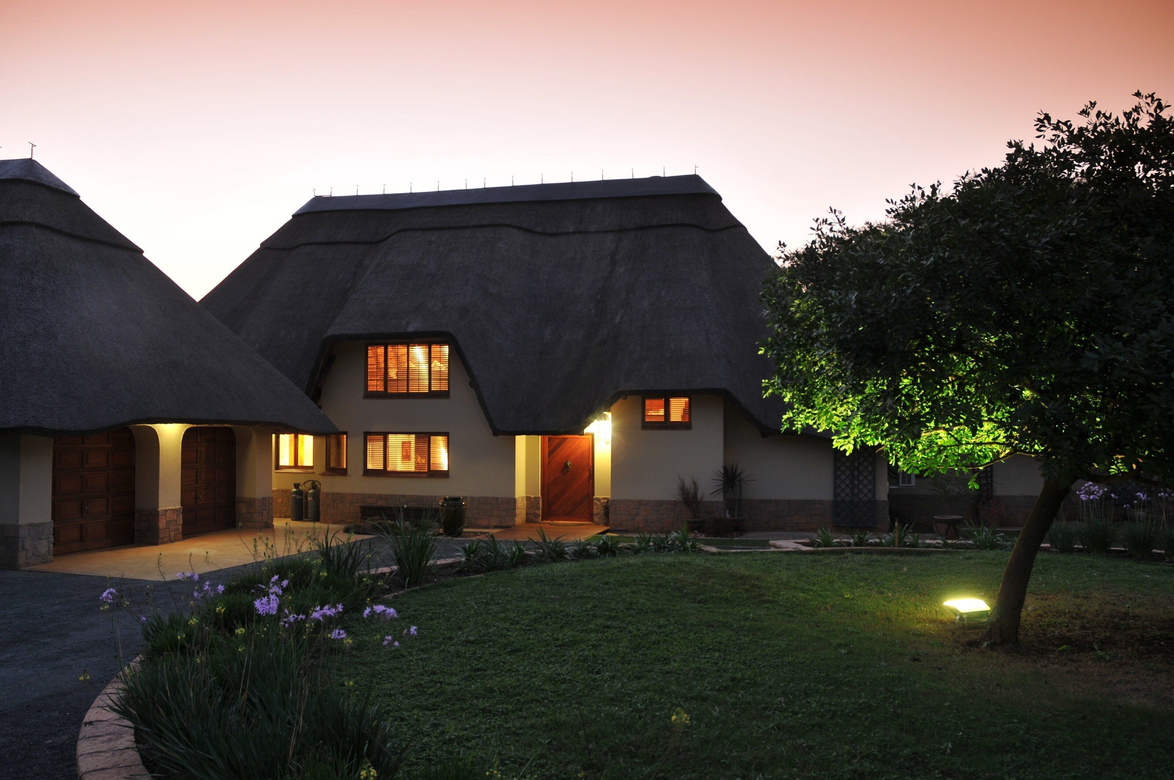 A house with a thatched roof, a well-lit entrance, and a garden with flowers.