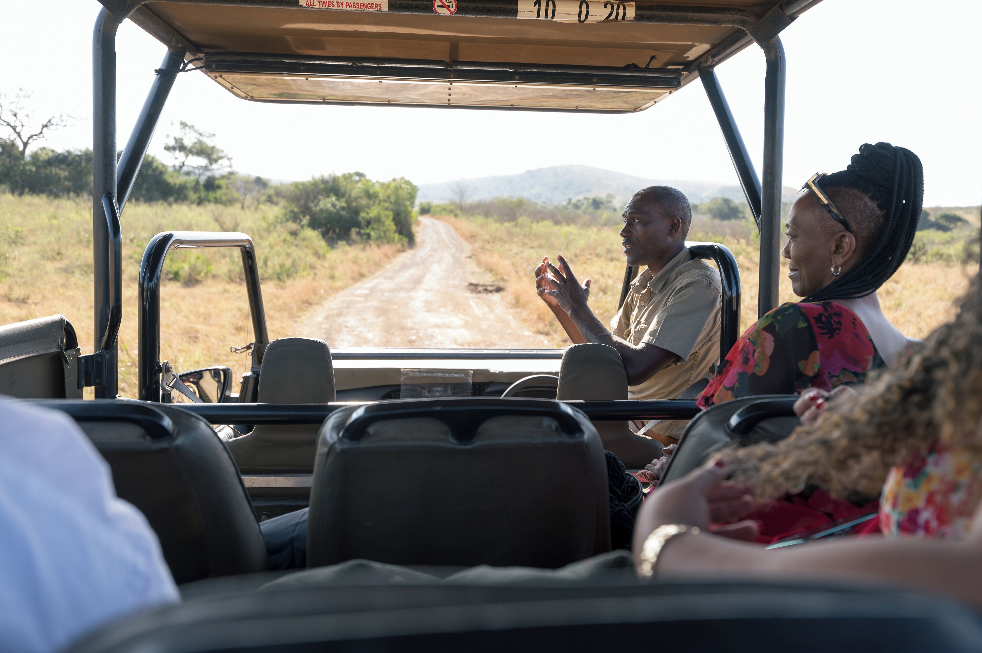 A safari vehicle interior with passengers, a steering wheel, and a view of a dirt road.