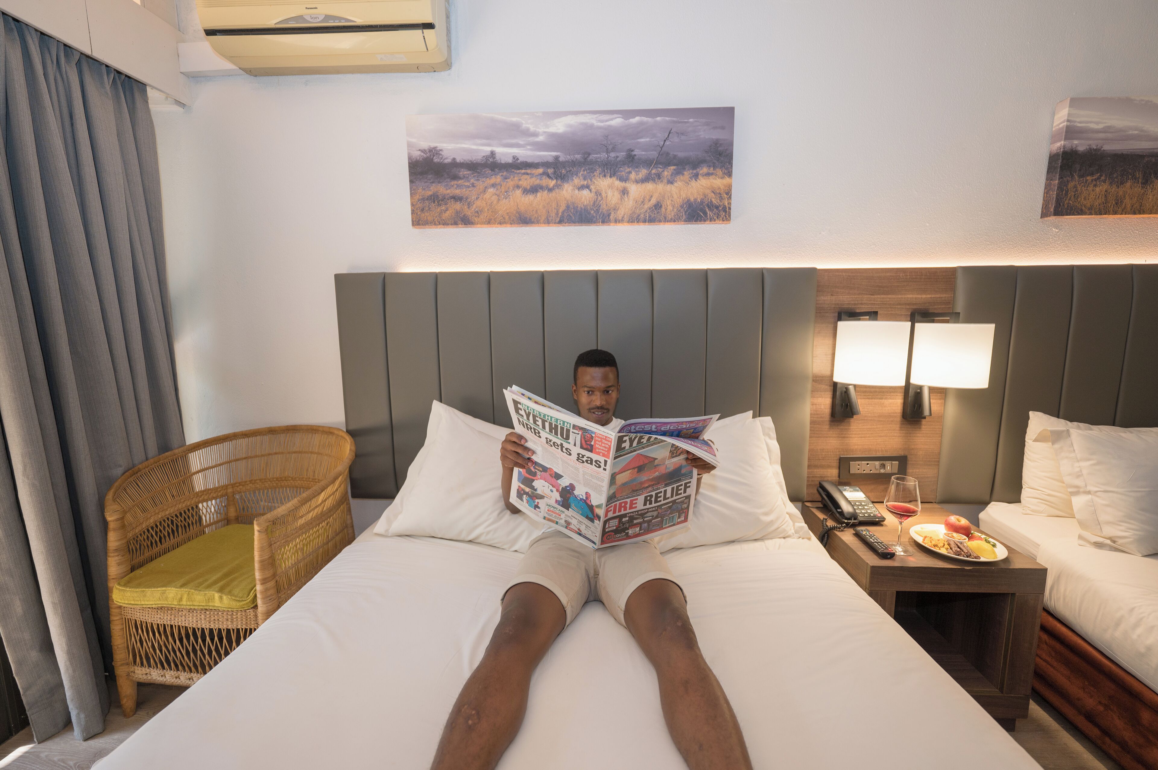 A hotel room with a bed, a reading chair, a bedside table with a lamp, and a wall-mounted painting.