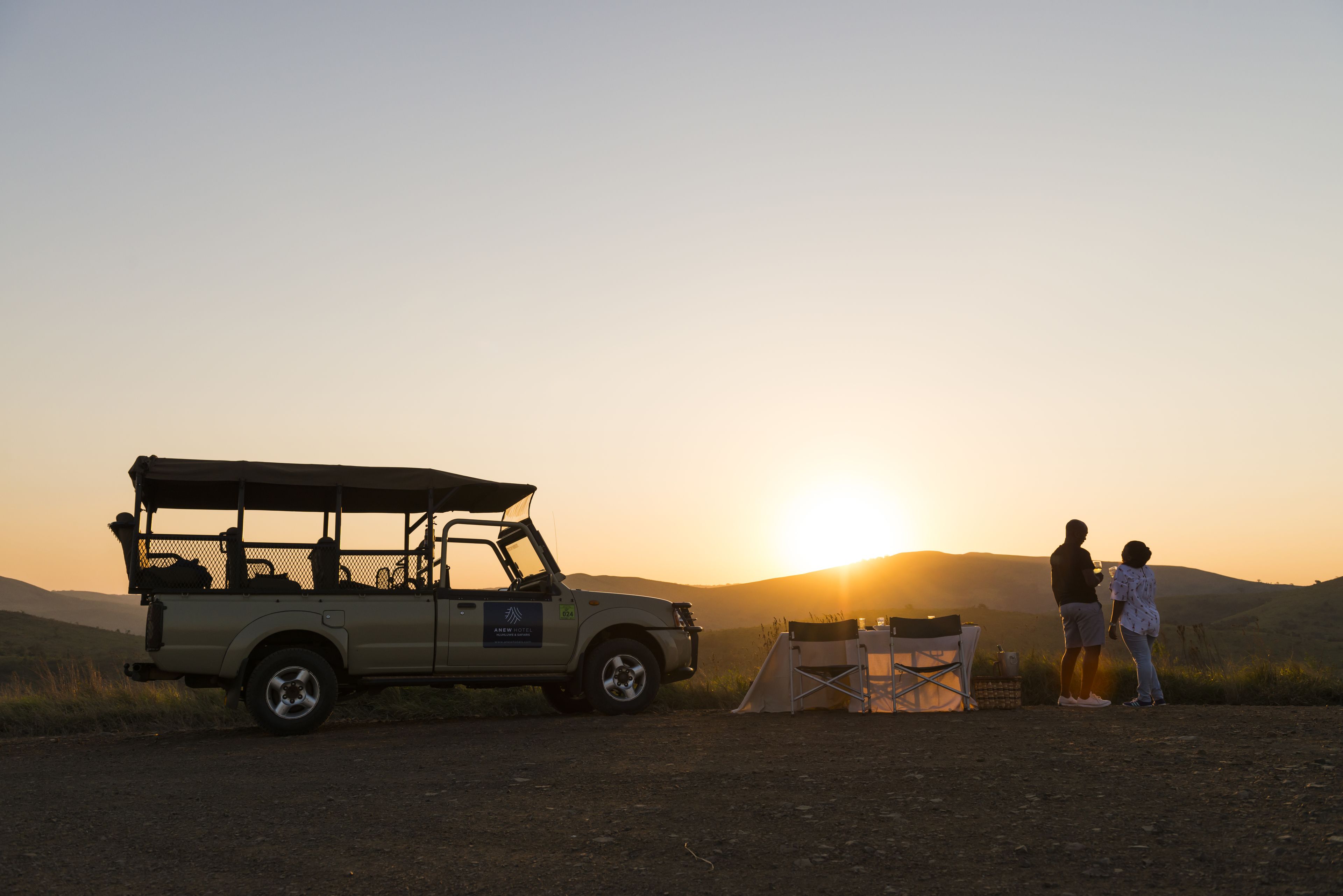 A safari vehicle parked on a dirt road with a tent and a chair nearby.