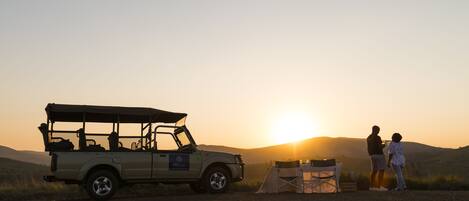 A safari vehicle parked on a dirt road with a tent and a chair nearby.