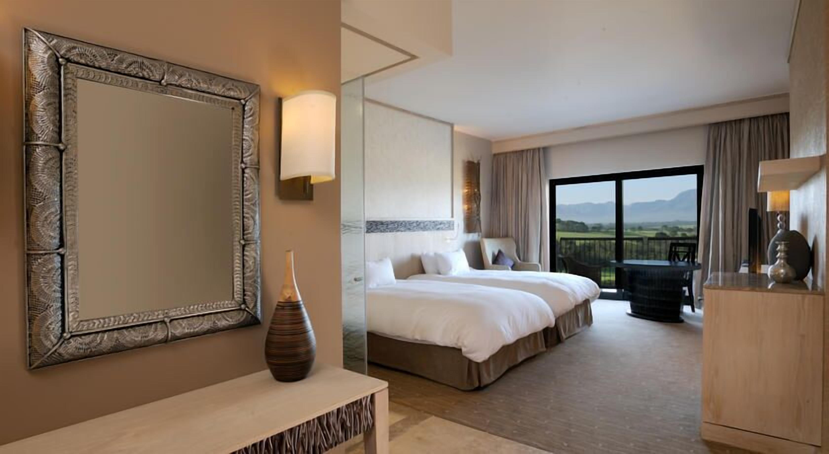 Een hotelkamer met een grote spiegel, een bed, een vaas, een bureau en uitzicht op de omgeving.