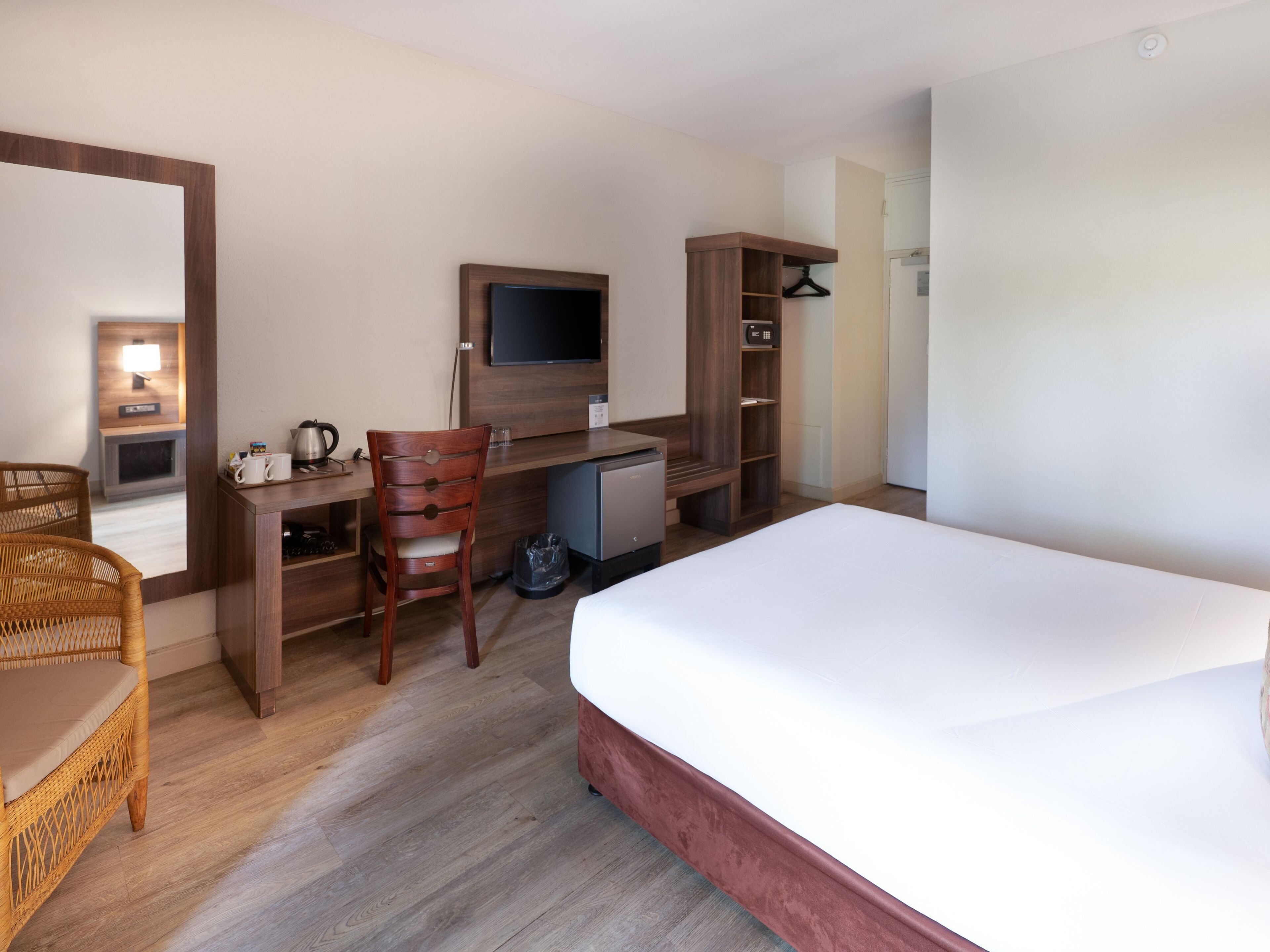 A hotel room with a bed, a desk, a chair, a TV, a wardrobe, and a small table with a lamp.