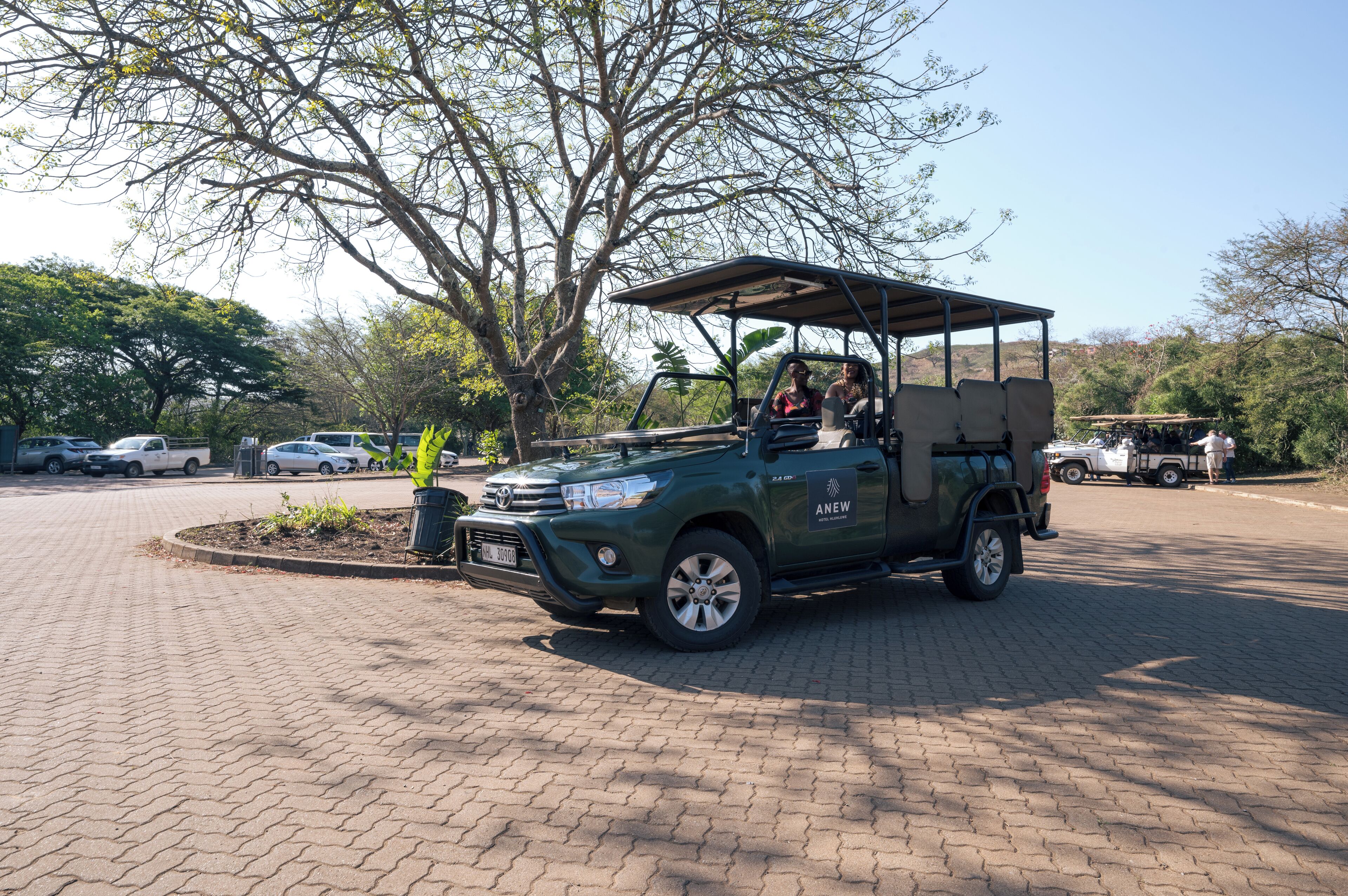 A green SUV with a roofed cargo area parked in a paved area with trees and other vehicles in the background.