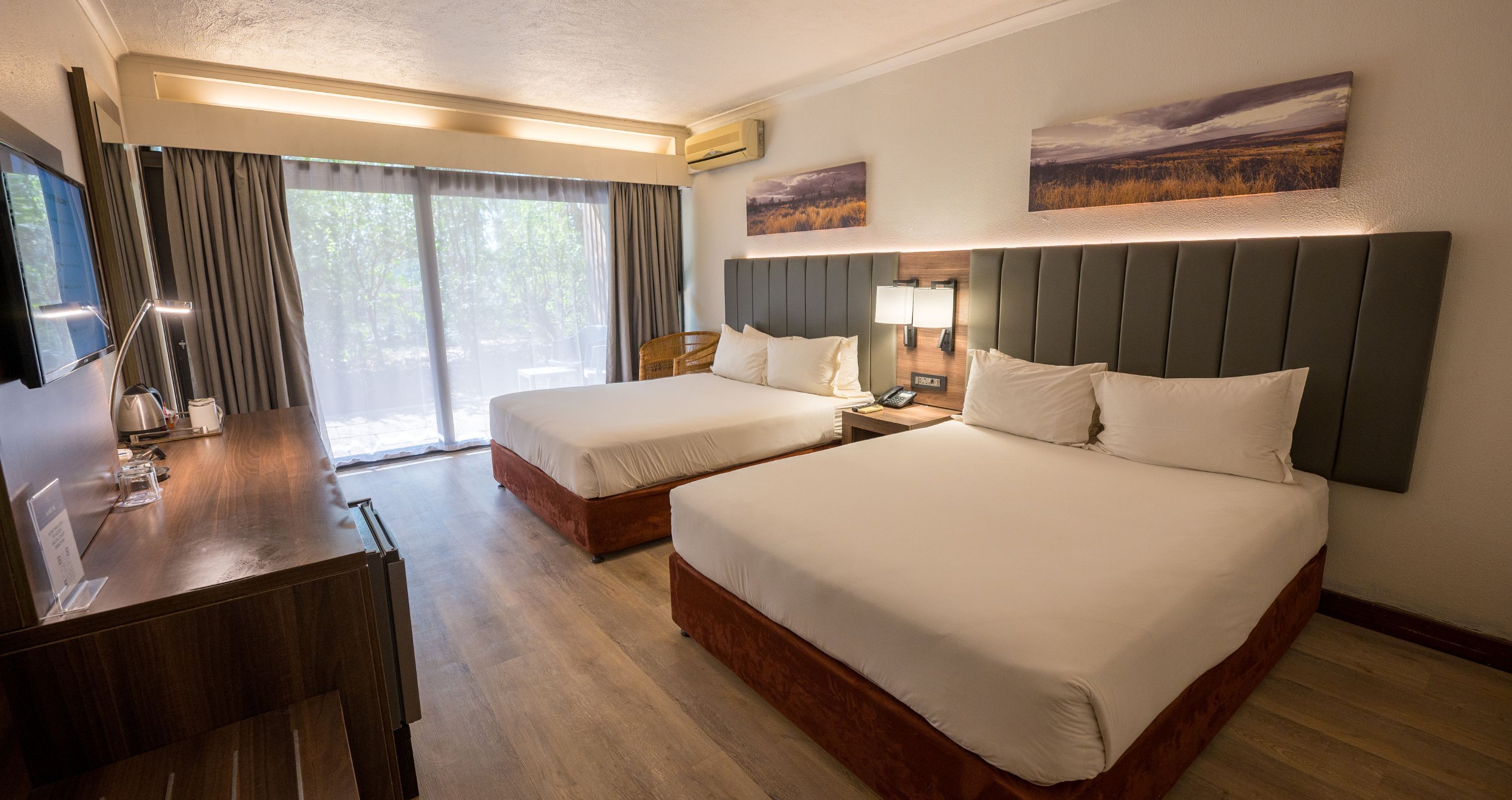 Une chambre d’hôtel avec deux lits, un bureau, une télévision et une fenêtre avec des rideaux.