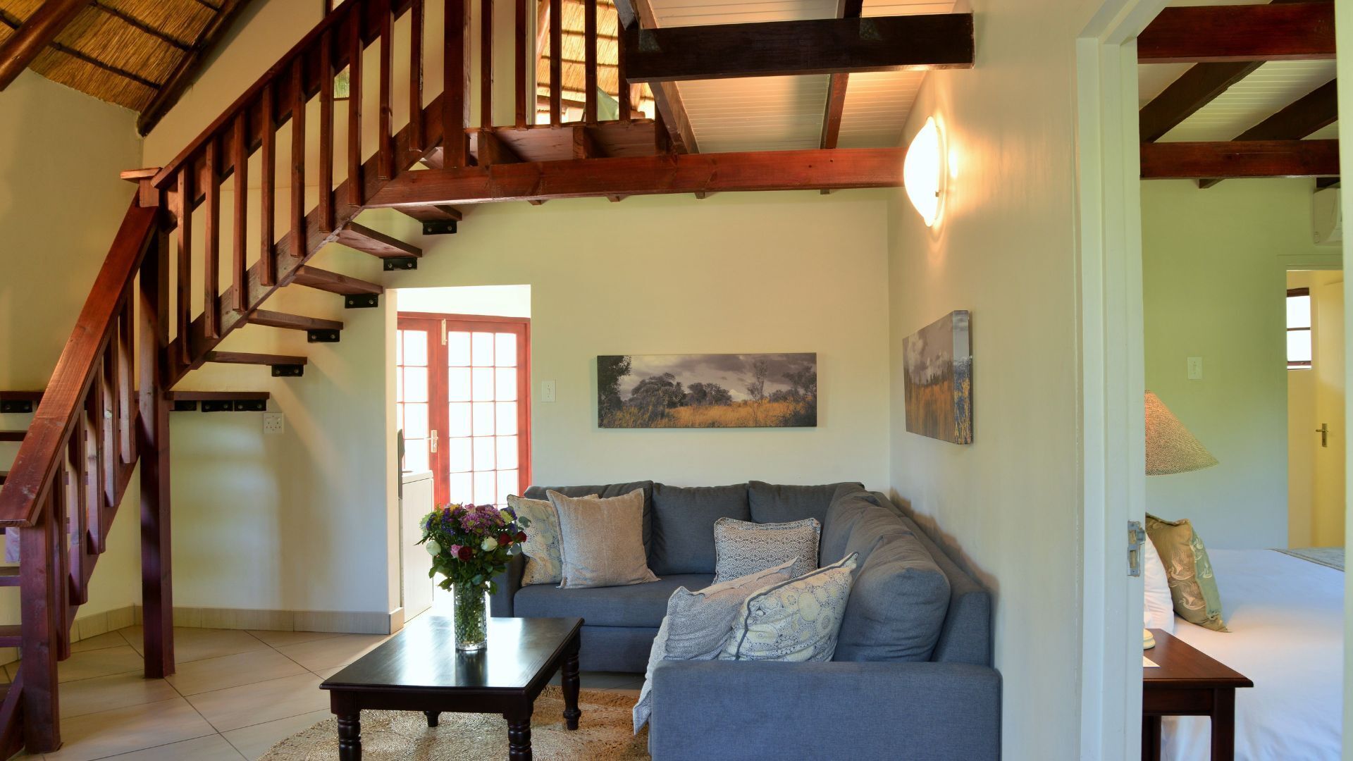 A living room with a staircase, a sofa set, a coffee table, and artwork on the walls.