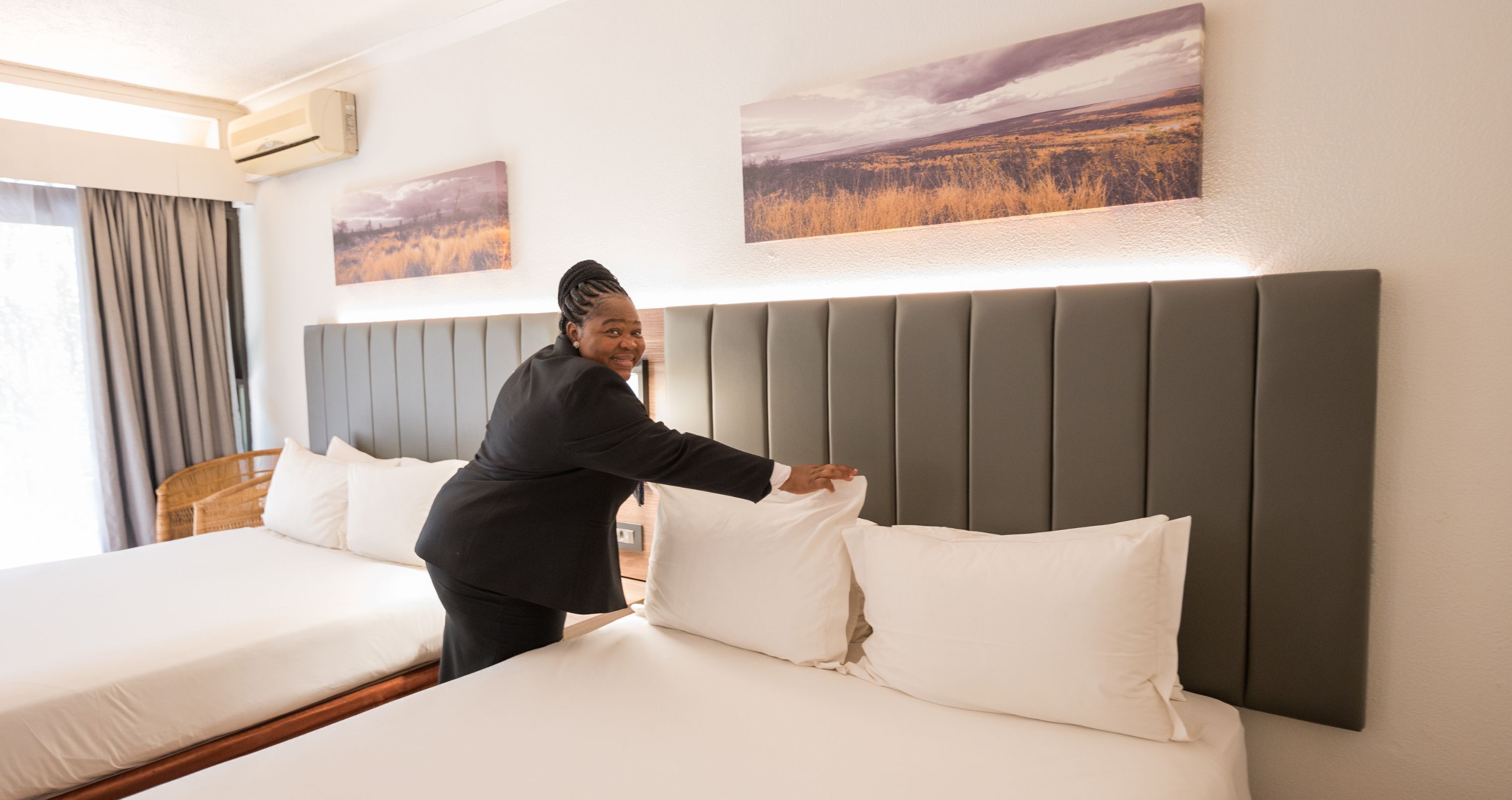 A hotel room with a large bed, a headboard, and two paintings on the wall.