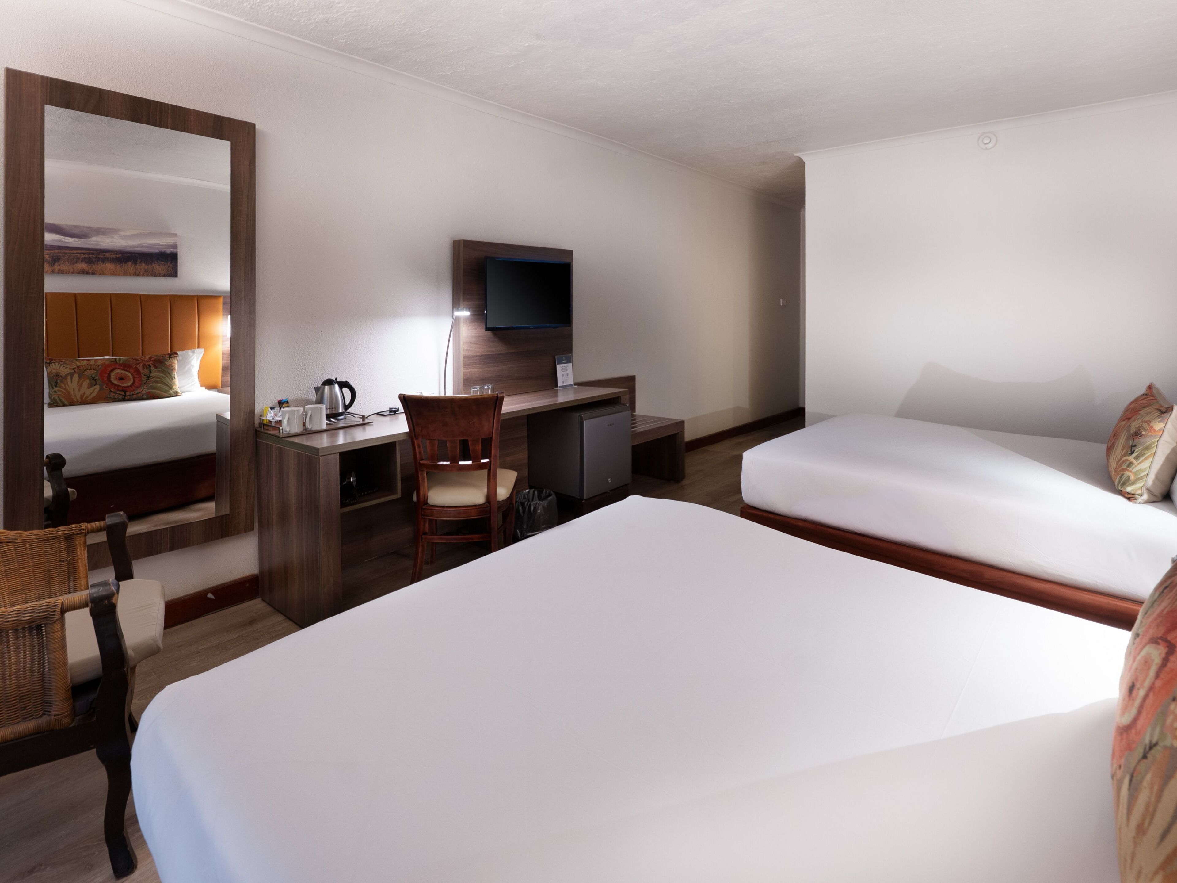 A hotel room with a large bed, a desk with a chair, a television, and a small kitchenette.