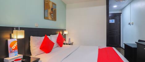Une chambre d’hôtel avec un lit, des tables de chevet, une lampe, un tableau au mur et une porte donnant sur une autre pièce.