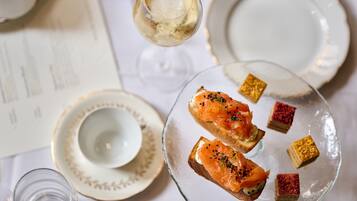 A table with a glass of white wine, a plate with smoked salmon on toast, and small square desserts.