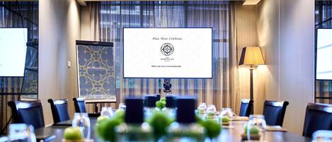 A conference room with a large screen displaying a welcome message, a table set with green apples, and a lamp.