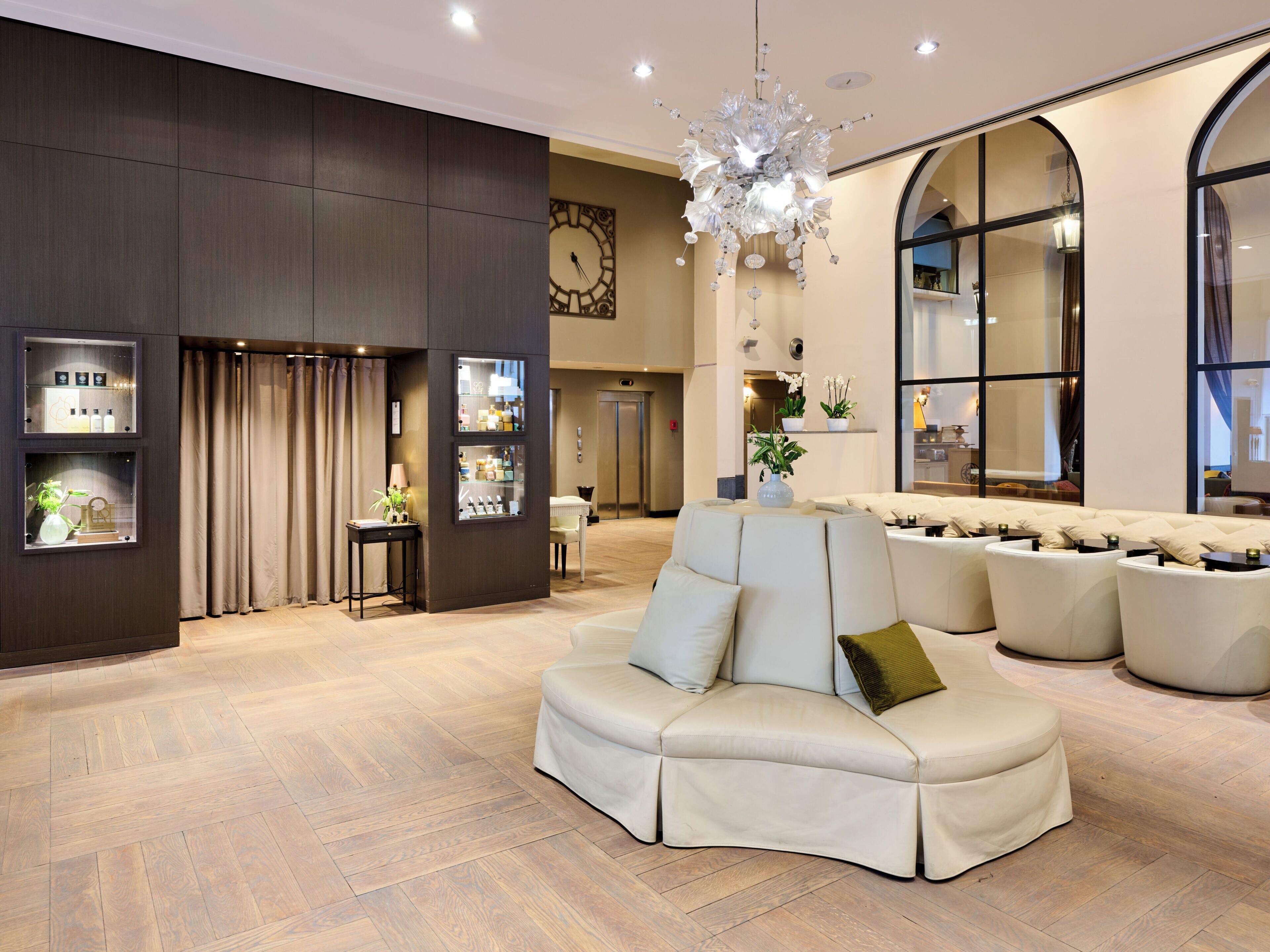 A spacious lobby with a large sofa, a chandelier, and a clock on the wall.
