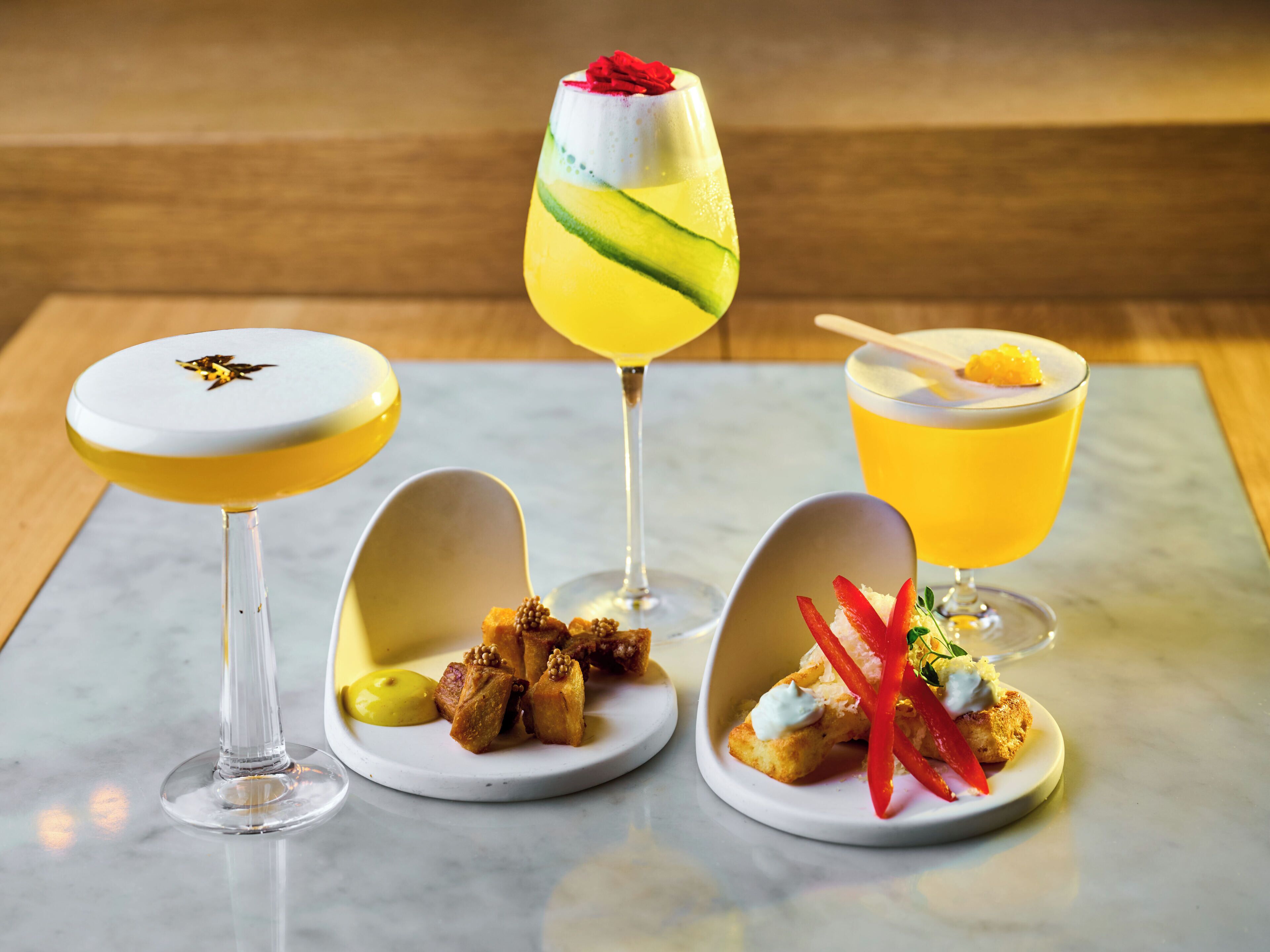 Three drinks and two plates of food on a marble table.