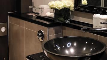 Un bany modern amb un lavabo negre, un ram de flors blanques i productes de tocador a la superfície.