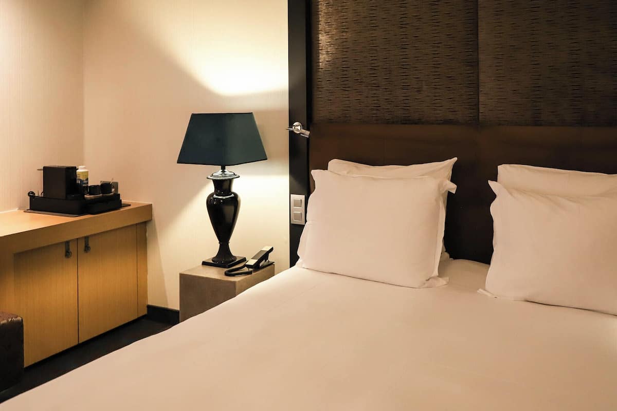 Une chambre d’hôtel comprenant un lit, une table de chevet avec une lampe, un petit meuble et un panneau fixé au mur.