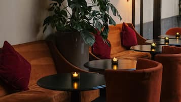 A cozy seating area with a large potted plant, red cushions, and small round tables with candles.