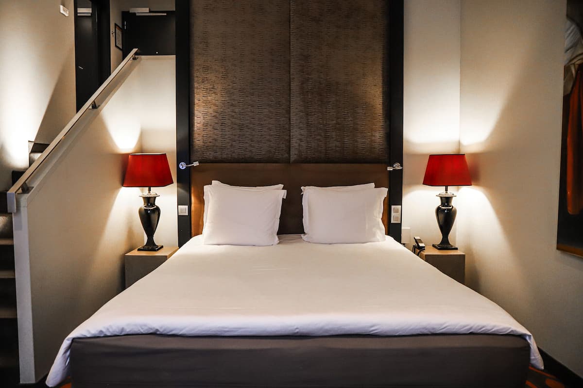 Une chambre d’hôtel avec un grand lit, deux lampes de chevet, une tête de lit en bois et un escalier.