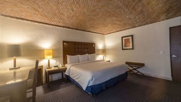 A hotel room with a large bed, a wooden headboard, two bedside tables with lamps, a small desk, and a chair.